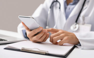 Consultation Online. Unrecognizable male doctor using smartphone at workplace, messaging with his patient, prescribing treatment